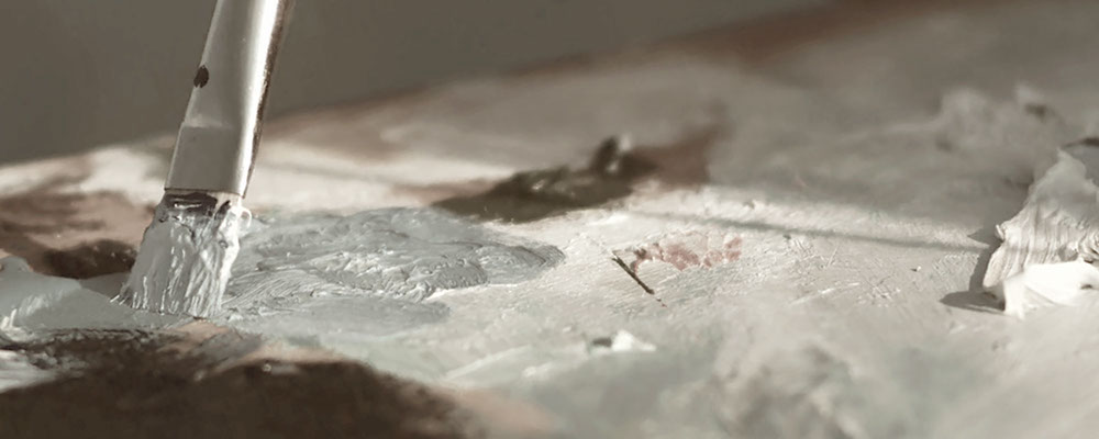 close-up photo of a paintbrush mixing paint on a wooden palette